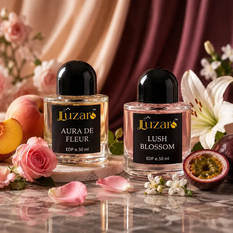 Luzaro Aura De Fleur and Lush Blossom perfumes surrounded by roses, peach, passionfruit, and flowers on a luxurious reflective surface.